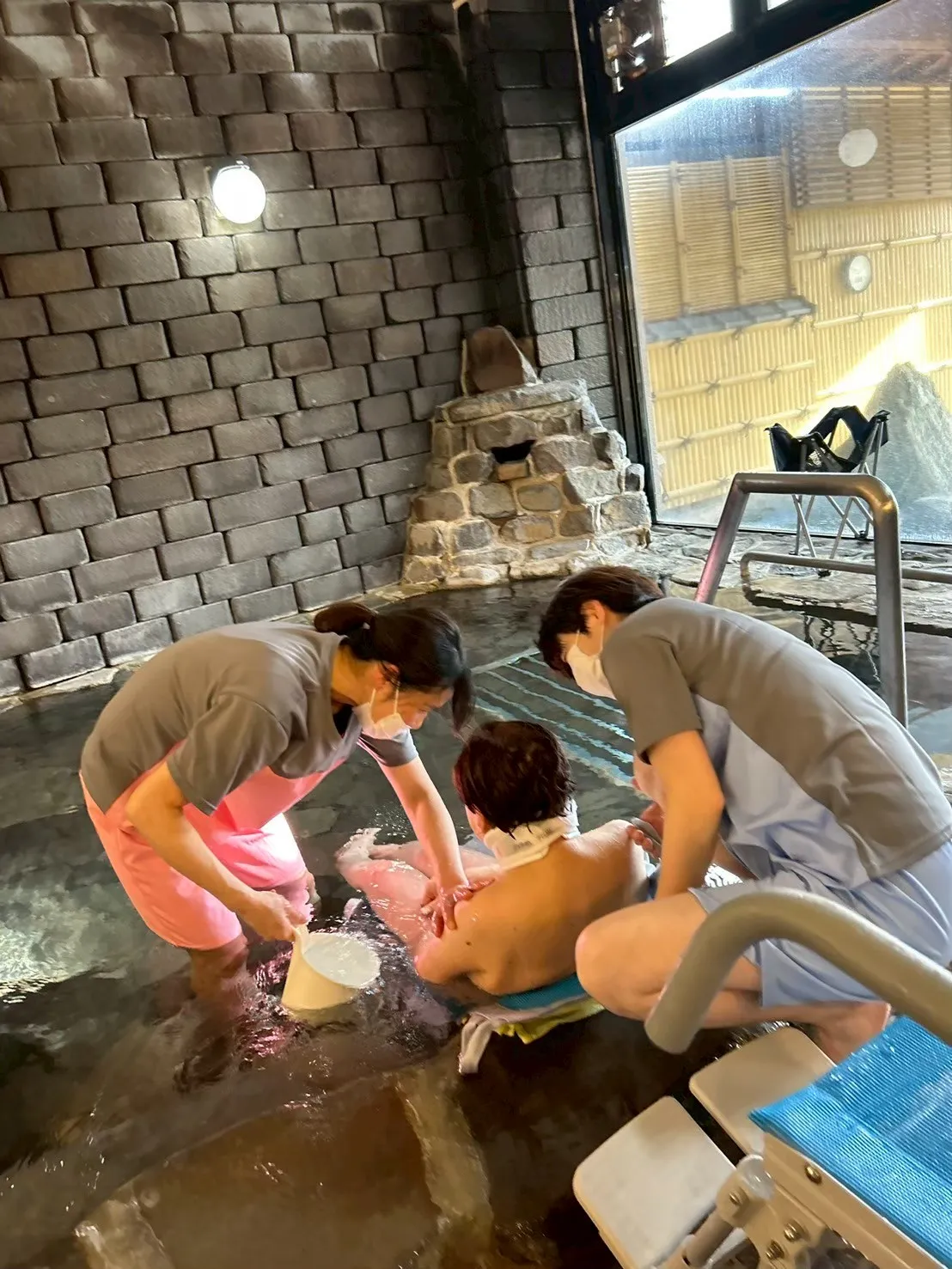 温泉で二名のヘルパーさんと入浴する人の画像