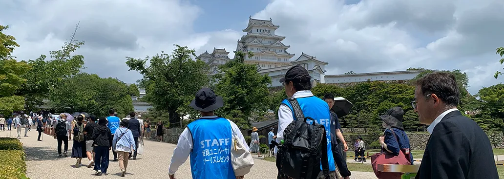 姫路城と、姫路ユニバーサルツーリズムセンターのスタッフが歩いている後姿の画像
