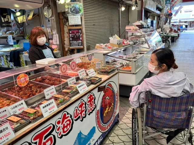魚の棚商店街を散策する車いすの女性の画像